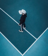 A person wearing a virtual reality headset stands on a large, empty sport court with distinct white lines on the floor. The dark clothing contrasts with the bright headset.